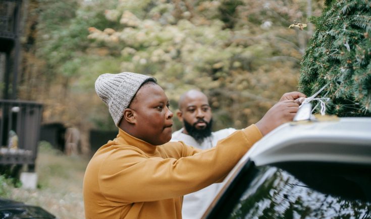 A father and son preparing for holidays by tying a Christmas tree onto a car roof. Outdoors in nature.